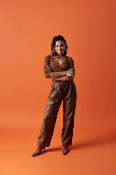 Une jeune femme pose en toute confiance dans un studio avec une toile de fond orange accrocheur, mettant en valeur sa tenue élégante. — Photo de stock