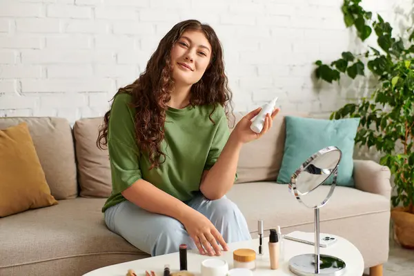 Uma jovem mulher com cabelo encaracolado relaxa em sua sala de estar, engajando-se em sua rotina de beleza com cosméticos ao redor. — Fotografia de Stock