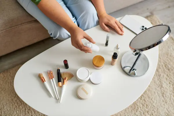 A cheerful young woman explores her beauty routine surrounded by various cosmetic products on a table. — Stock Photo