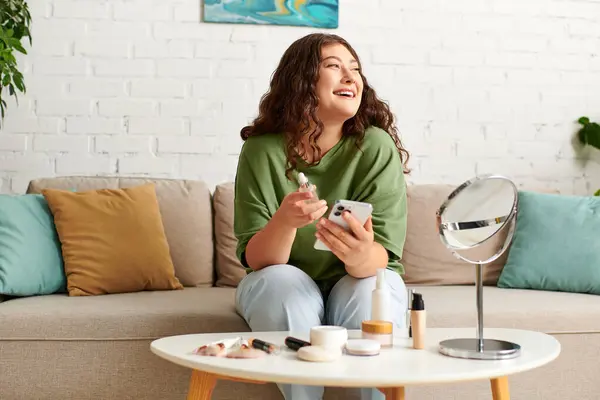 A cheerful curly-haired woman engages in her beauty routine, surrounded by makeup products in a cozy space. — Stock Photo