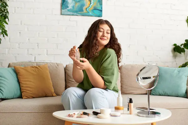 A young woman with curly hair relaxes in a casual outfit while applying her beauty products in a chic living room. — Stock Photo