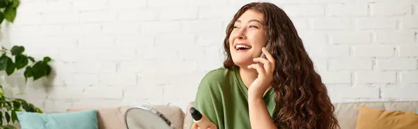 A cheerful plus-size woman with curly hair enjoys her beauty routine amid makeup in her cozy living space. — Stock Photo