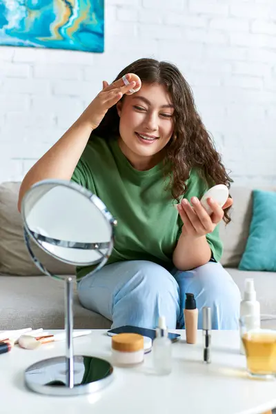 Uma jovem e encaracolada mulher plus size aplica produtos de cuidados com a pele em sua acolhedora sala de estar, desfrutando de seu ritual de beleza. — Fotografia de Stock