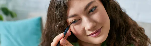 Eine junge Frau mit lockigem Haar schminkt sich in einem entspannten Wohnzimmer und umarmt ihre Beauty-Routine mit Freude. — Stockfoto