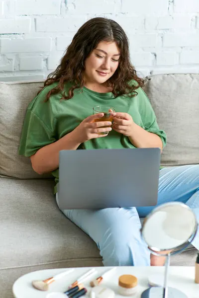 Une jeune femme joyeuse aux cheveux bouclés s'engage dans sa routine beauté tout en se relaxant avec des collations et un ordinateur portable. — Photo de stock