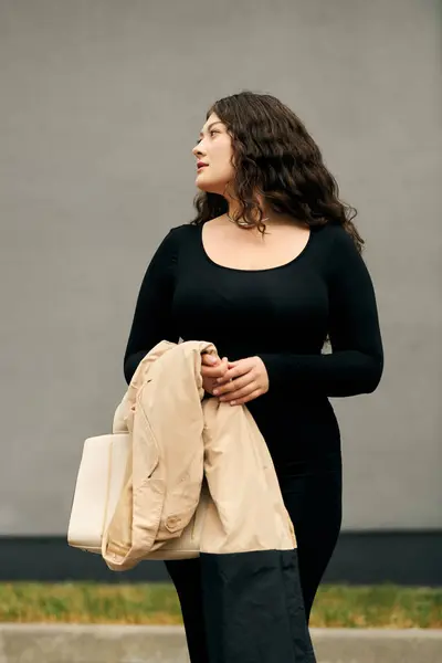 A young, beautiful woman embraces the autumn air in a black dress and chic beige trench coat. — Stock Photo