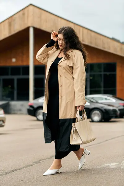 Una giovane donna plus size passeggia con fiducia in un abito nero e trench beige in una giornata autunnale. — Foto stock