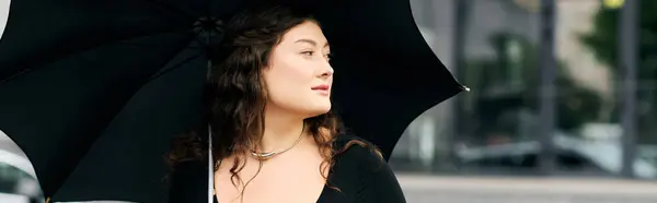 A young plus size woman enjoys a refreshing autumn stroll, adorned in a chic black dress while holding an umbrella. — Stock Photo