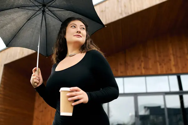 A beautiful plus size woman walks confidently outdoors, holding an umbrella and a warm drink on an autumn day. — Stock Photo