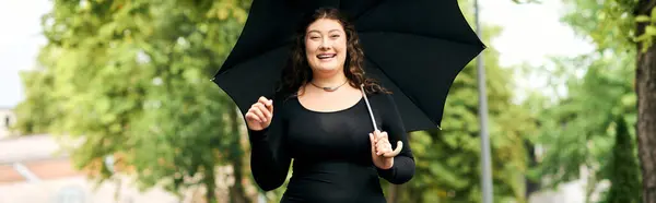 A beautiful plus size woman enjoys an autumn walk, smiling brightly while holding a black umbrella. — Stock Photo