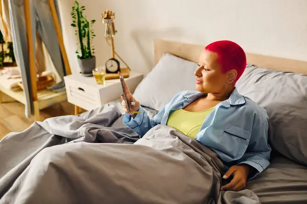 Cozy atmosphere as the young woman with vibrant hair unwinds in bed, immersed in her mobile device. — Stock Photo