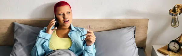 A young woman with vibrant hair chats on the phone while lounging in bed, enjoying her space. — Stock Photo