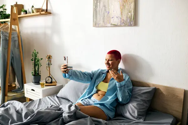 A young woman relaxes in bed, smiling and engaging in a lively video call during the morning. — Stock Photo