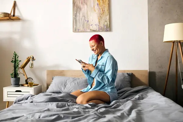 Una joven se relaja en su cama, sonriendo a su teléfono mientras está rodeada de un ambiente acogedor. - foto de stock