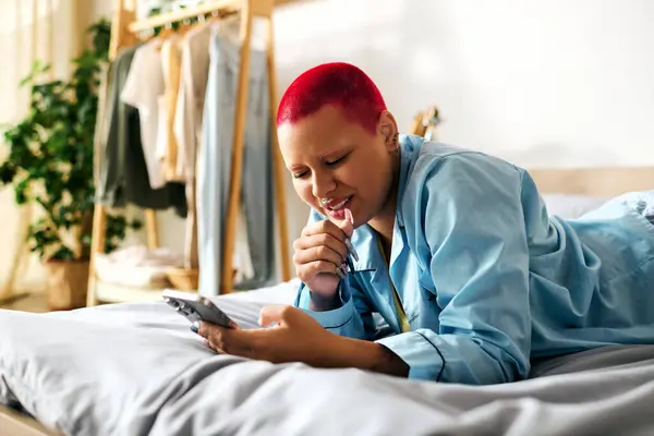 A young woman at home lounges on her bed, smiling while scrolling through her smartphone. — Stock Photo