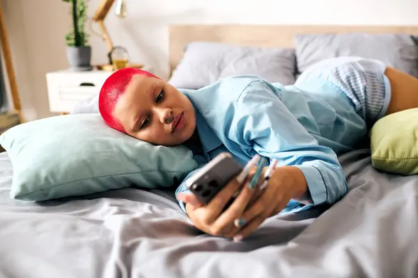 Una joven mujer se relaja en su cama, ocupada en su teléfono inteligente mientras descansa casualmente. - foto de stock