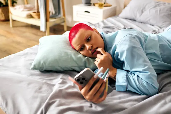 A vibrant young woman lounges comfortably on her bed, engaging with her phone and lost in thought. — Stock Photo