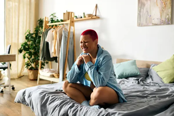 A young woman with red hair sits on her bed, smiling and enjoying a peaceful moment at home. — Stock Photo