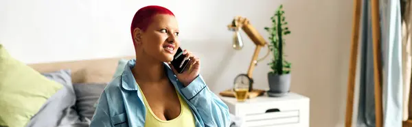 A cheerful young woman with vibrant red hair chats happily on her phone in her bedroom. — Stock Photo