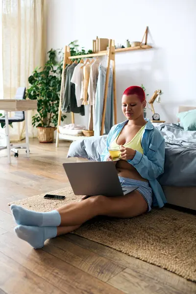 Relaxing at home, a young woman sips her drink while working on her laptop in cozy attire. — Stock Photo