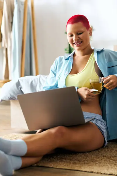 A young woman relaxes at home, sipping tea while engaged on her laptop, radiating joy and comfort. — Stock Photo
