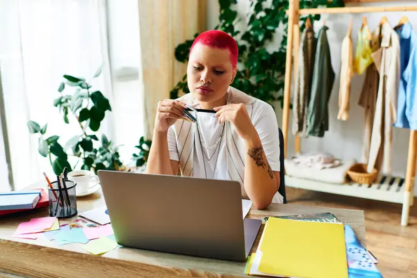 A young woman with bright hair focuses on work at her home desk, surrounded by plants. — Stock Photo