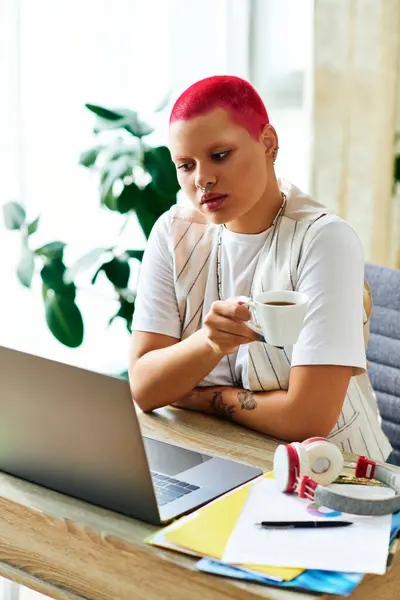 A young woman with vibrant hair sips coffee, focused on her laptop in a cozy workspace. — Stock Photo