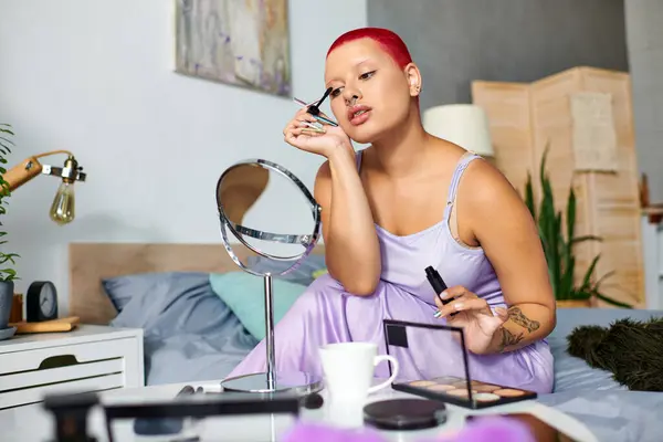 Una mujer joven se sienta en su cama, cuidadosamente aplicando rimel en su dormitorio elegante mientras se relaja. - foto de stock