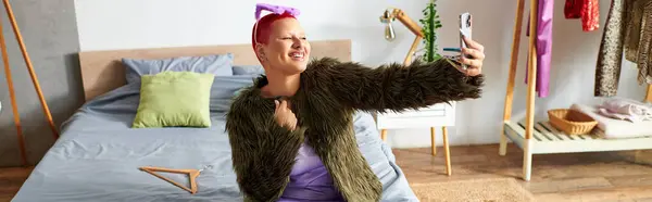 In a cozy bedroom, a young woman joyfully captures a selfie, showcasing her playful spirit. — Stock Photo