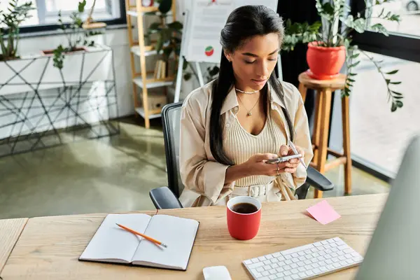In a modern office, a young woman concentrates on her smartphone while seated at her desk. — Stock Photo