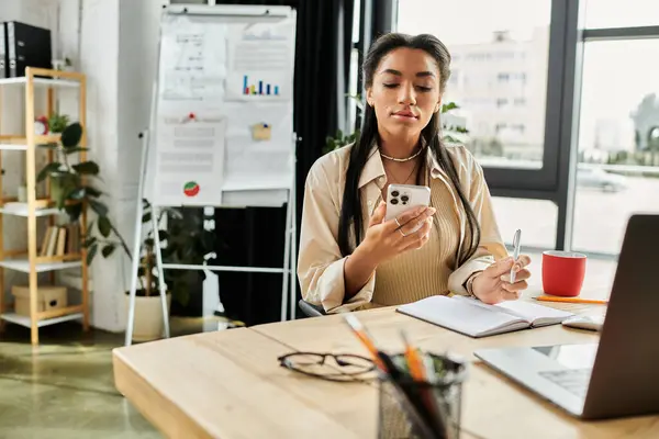 Una giovane donna alla sua scrivania medita i suoi prossimi passi, telefono in mano. — Foto stock