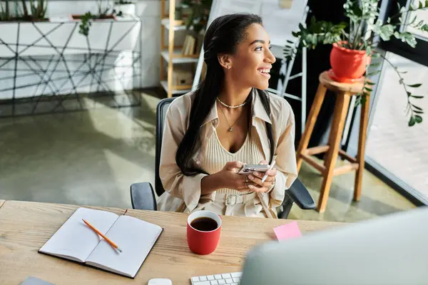 In un ufficio luminoso, una giovane donna si impegna felicemente con il suo smartphone sorseggiando un caffè. — Foto stock