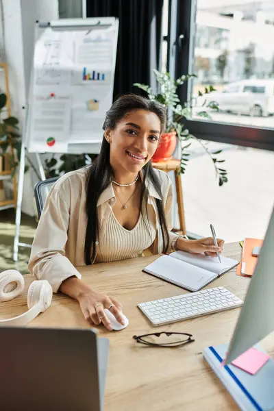 Una mujer joven se dedica enérgicamente a su trabajo en un escritorio lleno de suministros de oficina. - foto de stock