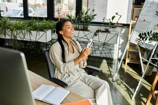 A young woman smiles while sitting in her modern office, using her phone and enjoying the moment. — Stock Photo