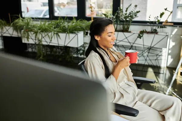 A cheerful young woman sips her drink, immersed in thought in a contemporary office setting. — Stock Photo
