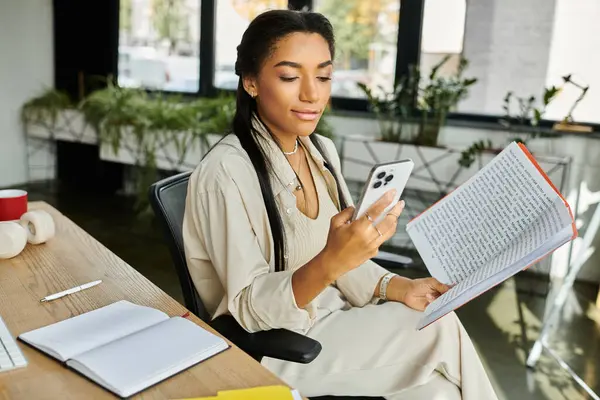A young woman reviews notes while texting, showcasing productivity in a vibrant workspace. — Stock Photo