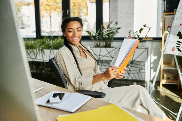 A cheerful young woman reviews documents in a bright, plant filled office. — Stock Photo