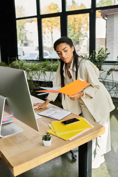 In a light filled workspace, a young woman sorts through colorful documents while working. — Stock Photo