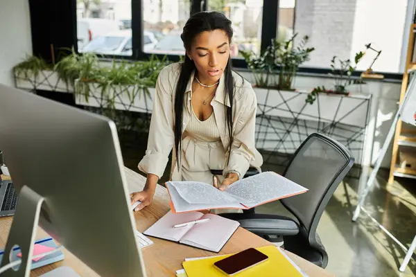 A focused young woman reviews important materials at her stylish office desk during work hours. — Stock Photo