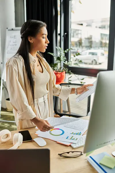 Una donna concentrata esamina grafici e dati aziendali in un ambiente di ufficio vibrante. — Foto stock