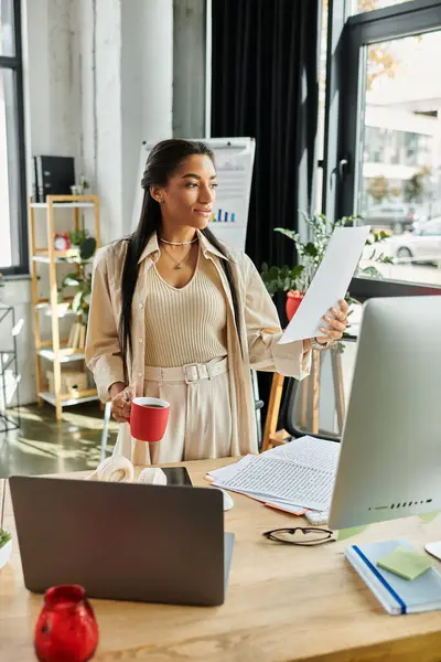 A young woman stands in a stylish office, examining important documents with a cup of coffee. — Stock Photo