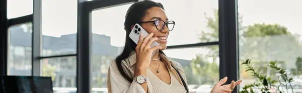 A young woman with glasses engages in a lively conversation on her phone, smiling. — Stock Photo