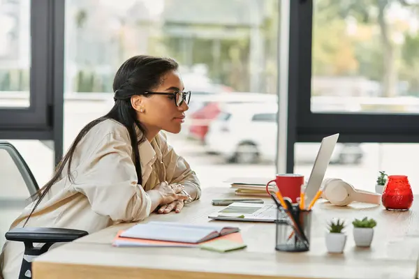 Eine junge Frau im hellen Outfit konzentriert sich auf ihren Laptop, umgeben von Bürodekoration. — Stockfoto