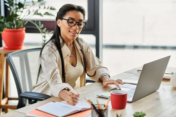 A confident young woman engaged in her tasks at a stylish office desk, showcasing productivity. — Stock Photo