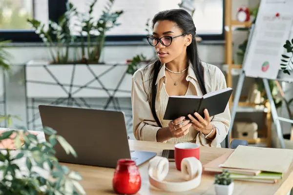 In a bright office filled with greenery, a focused woman writes in her notebook while working. — Stock Photo