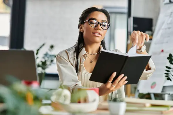 The young woman thoughtfully writes in her notebook while seated at her stylish office desk. — Stock Photo