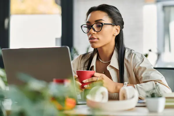 A professional young woman sips coffee while focused on her laptop, immersed in her work. — Stock Photo