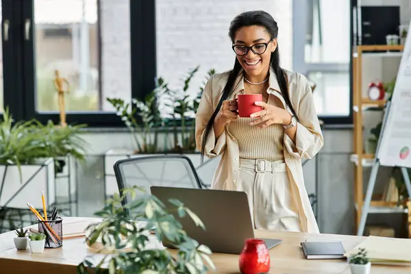 The beautiful woman smiles while holding a red mug, brightening her workspace with joy. — Stock Photo