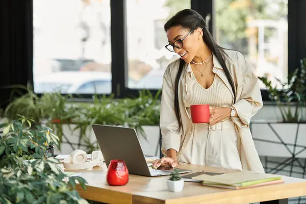 A cheerful woman collaborates on her laptop, sipping coffee in a vibrant, plant filled workspace. — Stock Photo