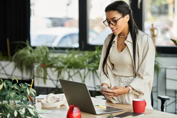 A young woman is actively working at her desk with a laptop and mobile phone in a stylish office. — Stock Photo